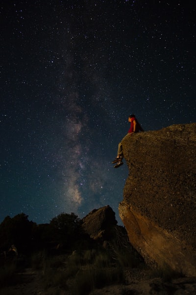 人坐在大岩石下边缘布满星星的夜空
